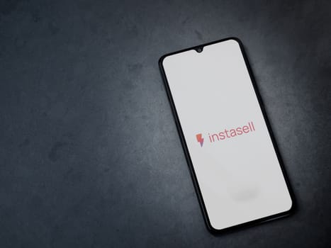 Lod, Israel - July 16,2023: Instasell app launch screen on smartphone on dark marble stone background. Top view flat lay with copy space.