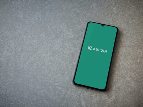 Lod, Israel - July 16,2023: KuCoin app launch screen on smartphone on ceramic stone background. Top view flat lay with copy space.