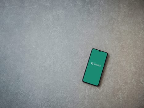 Lod, Israel - July 16,2023: KuCoin app launch screen on smartphone on ceramic stone background. Top view flat lay with copy space.