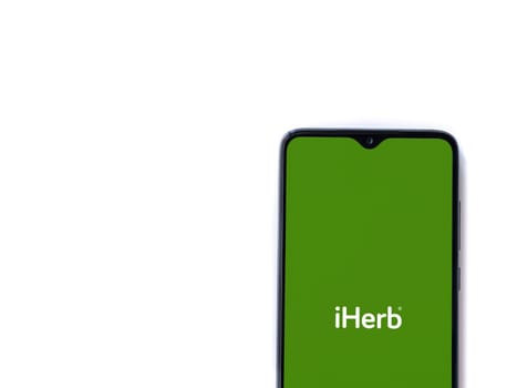 Lod, Israel - July 16,2023: iHerb app launch screen on smartphone on white background. Top view flat lay with copy space.
