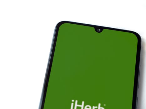 Lod, Israel - July 16,2023: iHerb app launch screen on smartphone on white background. Top view flat lay with copy space.