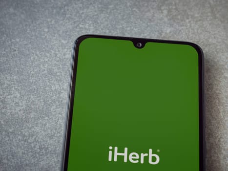 Lod, Israel - July 16,2023: iHerb app launch screen on smartphone on ceramic stone background. Top view flat lay with copy space.