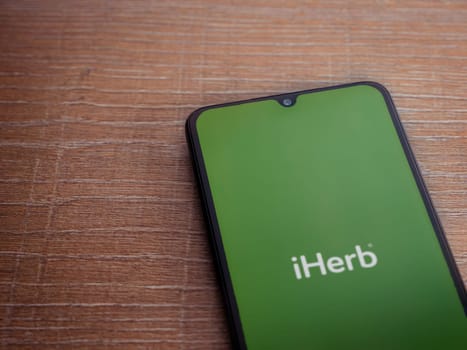 Lod, Israel - July 16,2023: iHerb app launch screen on smartphone on wooden background. Top view flat lay with copy space.