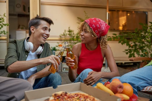 Outdoor picnic concept on weekend. Male and female teenage friends clinking beer bottles in camping