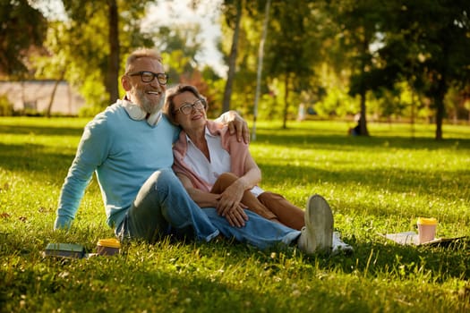 Happy loving romantic couple embracing while rest on grass in park. Relaxed mature spouses hugging together feeing romance mood