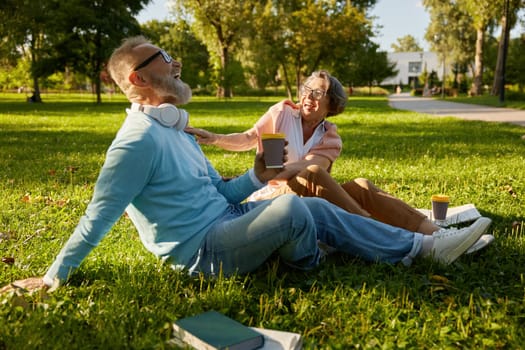Senior loving family drinking coffee and laughing while relaxing on green lawn grass outdoors in park