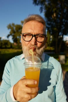 Closeup face portrait of old senior man drinking cool refreshment cocktail from straw in takeaway couple. Hot summer day and active walk of retired male in public park