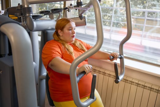 Tired sweaty obese woman breathing hard training at gym with sports equipment. Slimming and health care concept