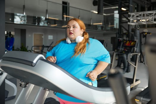 Active overweight woman running on treadmill track enjoying cardio exercise for calorie burning. Sportive challenge for slimming