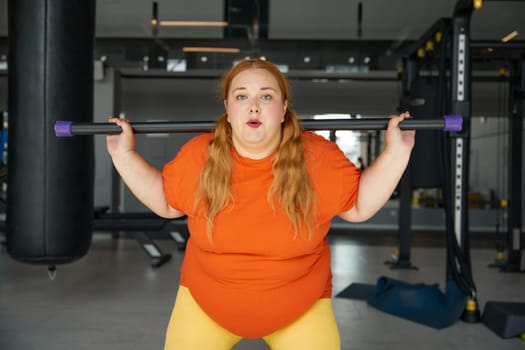 Overweight woman having fitness workout squatting with body bar training equipment. Obese girl exercising for being strong, slim and healthy