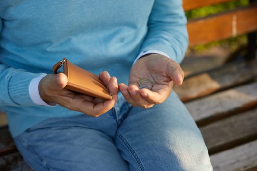Crop shot of male hands counting money coins from the wallet while sitting on bench. Pensions living minimum, poverty, low income and austerity in old age concept