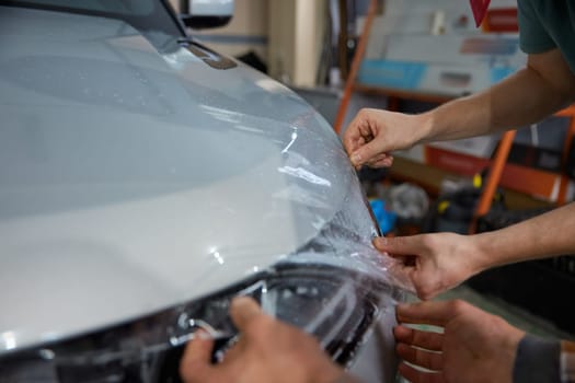 Closeup repairman hands smoothing protective film on car headlights in garage service station