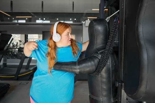 Motivated fat woman doing punching exercises boxing at gym. Plus size sporty female enjoying fitness workout to lose weight