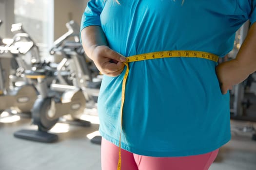 Closeup waistline of chubby woman wrapped in measuring tape. Workout sport and slimming program for people with obesity