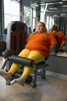 Beautiful chubby girl sportive outfit training at gym doing legs pump exercises on sports equipment