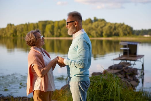 Senior husband confessing his love to wife during walk near river in public park or countryside. Spouses bonding and loving relationship throughout life, golden wedding