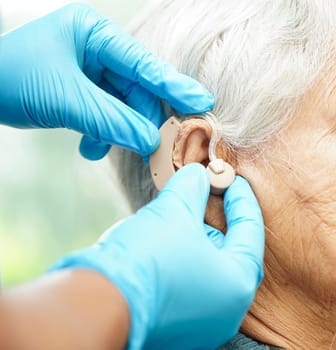 Asian senior woman patient using hearing aid in ear to reduce hearing loss problem.