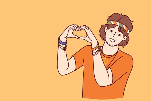 Hippie man demonstrates heart gesture made from fingers and smilingly looks at screen calling for pacifism and kindness. Romantic guy promotes philosophy of pacifism and calls not to quarrel