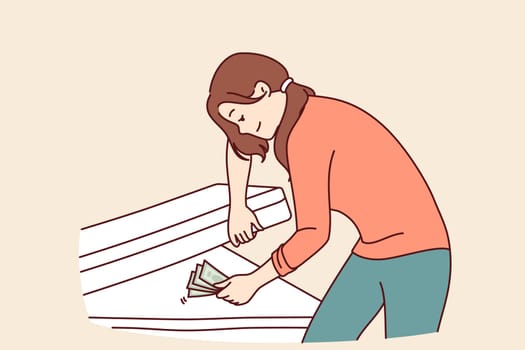 Woman hides money under mattress and smiles, keeping money safe and wanting to save up for big purchase. Concept of lack of financial literacy in girl who does not trust bank deposits