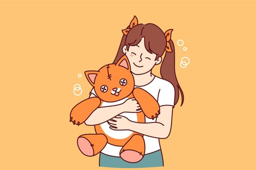 Little girl holds plush cat and smiles and rejoices at presence of favorite toy. Positive child with toy given by mom or dad enjoys hugging kitten for concept of happy childhood for daughter