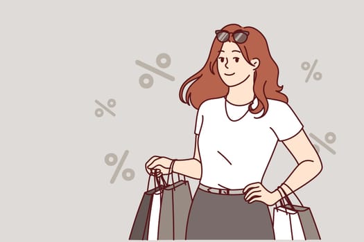 Woman shopaholic returns from store with packages and stands among percent symbols. Shopaholic girl smiles, rejoicing at opportunity to go shopping and visit fashion boutiques with clothes.