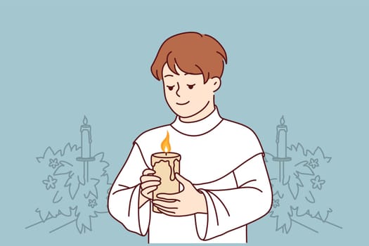 Boy participates in holy communion and holds burning candle for christian religious ritual in church. Child in clothes for communion ceremony in church smiles, wanting to become true believer catholic