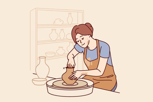 Woman sits in pottery workshop and sculpts jug from clay to sell handmade souvenirs in craft goods shop. Girl craftsman is interested in pottery art, dressed in apron stained with dirt.