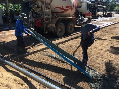 SURATTHANI, THAILAND - 12 May 2023 : Workers are unloading cement from trucks and spreading it around the area, This is the process of pouring cement to create a concrete road.