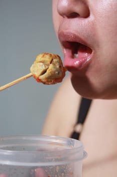 Woman happily eating meatball on gray blurred background