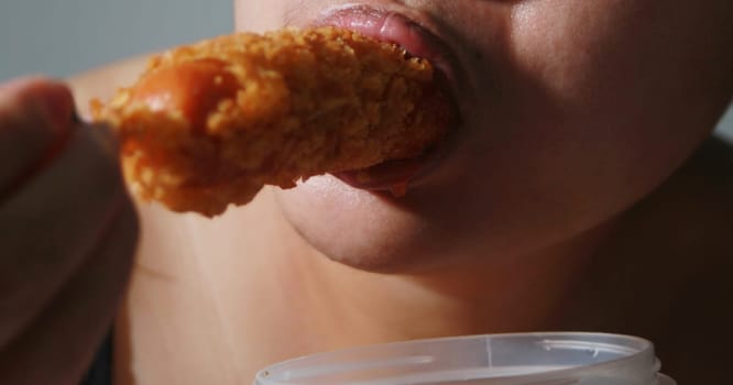 Woman happily eating sausage on gray blurred background