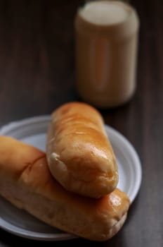Bread on a white plate sits on a wooden board table with milk in a bottle behind it, Copy space, Blurred background