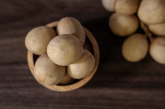 Langsat Longkong is a fruit found in the forests of tropical countries in Asia. And it is a fruit with a delicious aroma that is popular in Thailand, Malaysia, Singapore, Indonesia, Laos and Vietnam. Langsat Longkong is placed in a wooden cup on a dark wooden plank table with a blurred background.