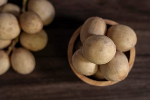 Langsat Longkong is a fruit found in the forests of tropical countries in Asia. And it is a fruit with a delicious aroma that is popular in Thailand, Malaysia, Singapore, Indonesia, Laos and Vietnam. Langsat Longkong is placed in a wooden cup on a dark wooden plank table with a blurred background.