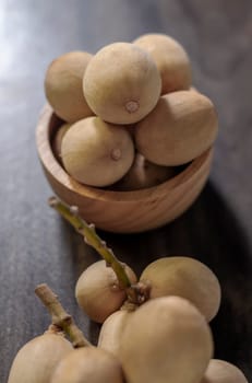 Langsat Longkong is a fruit found in the forests of tropical countries in Asia. And it is a fruit with a delicious aroma that is popular in Thailand, Malaysia, Singapore, Indonesia, Laos and Vietnam. Langsat Longkong is placed in a wooden cup on a dark wooden plank table with a blurred background.