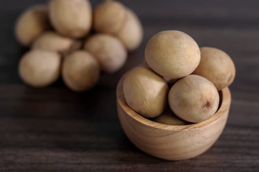 Langsat Longkong is a fruit found in the forests of tropical countries in Asia. And it is a fruit with a delicious aroma that is popular in Thailand, Malaysia, Singapore, Indonesia, Laos and Vietnam. Langsat Longkong is placed in a wooden cup on a dark wooden plank table with a blurred background.