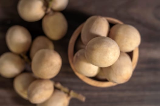 Langsat Longkong is a fruit found in the forests of tropical countries in Asia. And it is a fruit with a delicious aroma that is popular in Thailand, Malaysia, Singapore, Indonesia, Laos and Vietnam. Langsat Longkong is placed in a wooden cup on a dark wooden plank table with a blurred background.