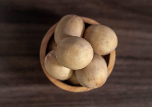 Langsat Longkong is a fruit found in the forests of tropical countries in Asia. And it is a fruit with a delicious aroma that is popular in Thailand, Malaysia, Singapore, Indonesia, Laos and Vietnam. Langsat Longkong is placed in a wooden cup on a dark wooden plank table with a blurred background.