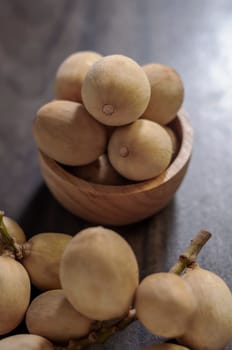 Langsat Longkong is a fruit found in the forests of tropical countries in Asia. And it is a fruit with a delicious aroma that is popular in Thailand, Malaysia, Singapore, Indonesia, Laos and Vietnam. Langsat Longkong is placed in a wooden cup on a dark wooden plank table with a blurred background.