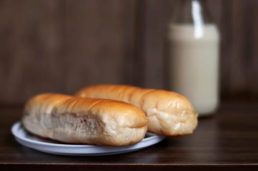 Bread on a white plate sits on a wooden board table with milk in a bottle behind it with copy space. Blurred background