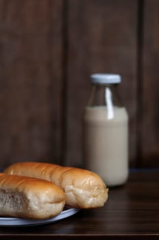 Bread on a white plate sits on a wooden board table with milk in a bottle behind it. Blurred background