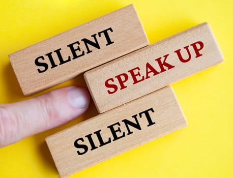 Finger pointing at wooden block with word speak up on yellow cover background. Courage to speak up concept.