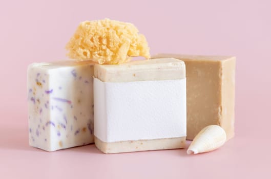 Beige handmade soap bars with blank label, natural sponge and seashell on light pink close up, packaging mockup, copy space. Herbal products for face and body care