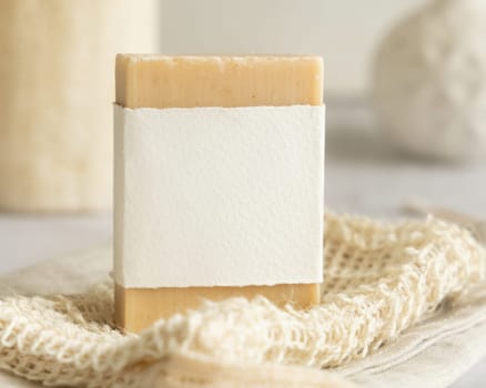 Beige handmade soap bar with blank label on soap saver bag on wooden table, packaging mockup, copy space. Natural herbal products for face and body care