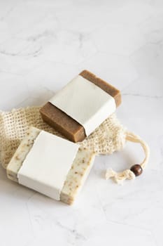 Beige handmade soap bars with blank label on sisal soap saver bag on marble table close up, mockup, copy space. Natural herbal products for face and body care.