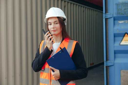 Female Foreman using walkie talkie radio and clip folder, control loading containers box