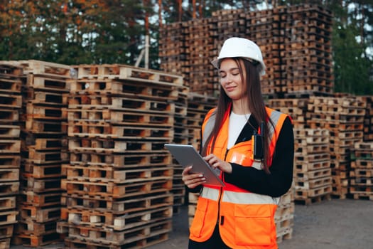 Woman engineer in white helmet with tablet at outdoors warehouse with pallets speak on phone