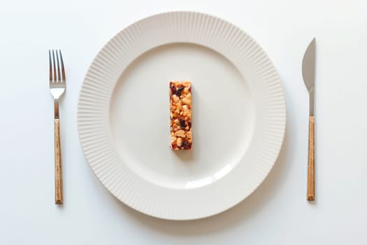 One muesli bar in the dish. Fork and knife on white. Energy cereal food, diet concept