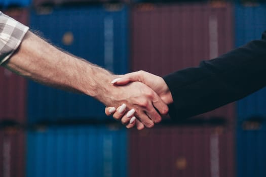 People at work: man and woman hand shaking at shipping terminal with containers in background.