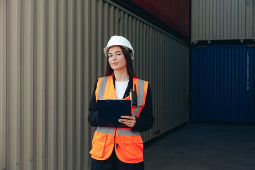 Female Engineer with Clip Folder in white helmet and vest working in container terminal port or construction site.
