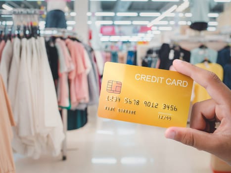 Human hand holding a credit card inside a shopping mall It represents the concept of online shopping and the concept of cashless spending.